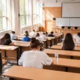 Students sitting at desks in a large lecture hall taking an exam with papers and water bottles