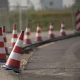 O serie de conuri de trafic alb-roșii așezate în linie de-a lungul marginii unui drum proaspăt asfaltat, delimitând o zonă de lucru