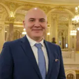 Portrait of a smiling bald man in a suit standing in front of a Gala Premiilor MUSICRIT backdrop